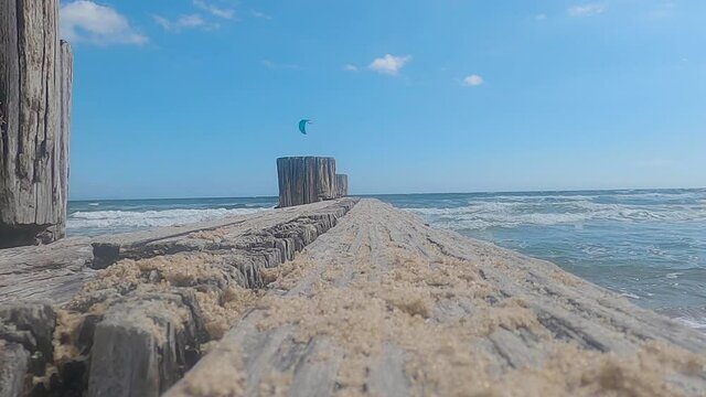 An old eroding wharf at the beach with a Kiteboard or kitesurfing in the distance