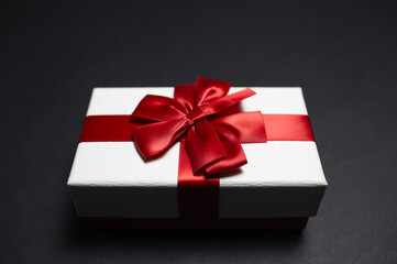 Close-up of white gift box with red ribbon bow on black background.
