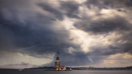 Fototapeta premium A long exposure cloudscape of a stormy sky above a sea with a tower on a small island in the foreground. Big Islamic city in the background. Slightly blurred grey clouds, blurred water. No people.