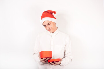 New Year's photo. A man in a santa hat on a white background holds a box in his hands, the guy looks into an empty box, there is no money for a gift