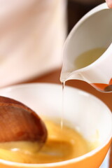 Pouring oil to an egg yolk. Making mayonnaise with a wooden spoon.