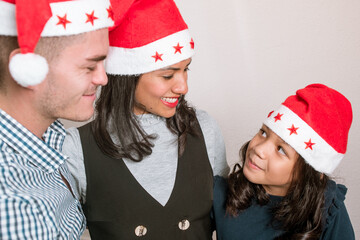 Young family looking to each other celebrating christmas time together wears red santa hat.