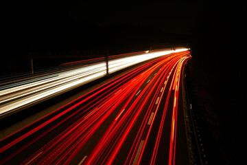 highway traffic at night in a right curve with red white yellow lights and a toll bridge