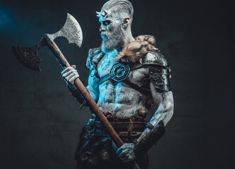 Naked and pale skinned god with horns and blue eyes holding two handed axe and looking at it in...