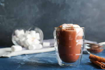Glass of hot cacao drink with marshmallows on color background