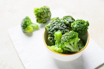 Bowl with frozen broccoli on light background