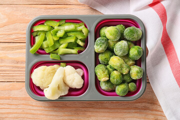 Divided box with different frozen vegetables on wooden background