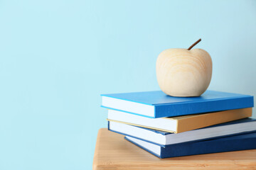 Stack of books and wooden apple on table near color wall