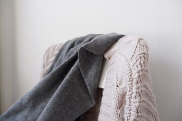 Knitted gray sweater and wool shawl on the back of a white wooden chair. ニットガーディガンとショールのかかる椅子