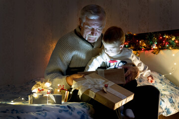 Fototapeta na wymiar grandfather and grandson open a New Year's gift, inside a glowing magic surprise illuminates them with a fabulous golden light. New year, christmas with family