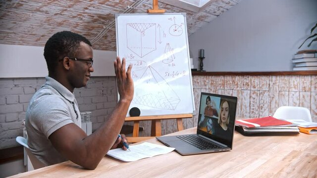 An online maths lesson - an african-american man teacher in glasses greeting his students on the screen