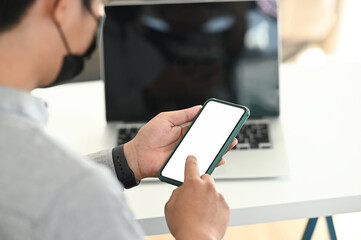 Cropped shot of a male hand using blank screen mobile  phone at his work space.