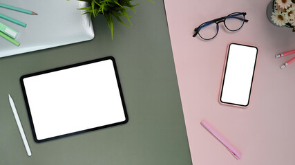 Top view of feminine stylish office desk with copy space, tablet,smart phone, glasses, and decoration on two tone background.