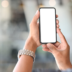 Cropped shot of man hands holding mobile phone with white screen on blured office room background.