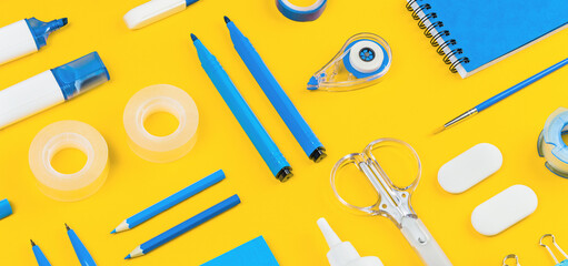 Assorted office and school white and blue stationery on bright yellow background. Organized knolling for back to school or education and craft concept. Banner wide