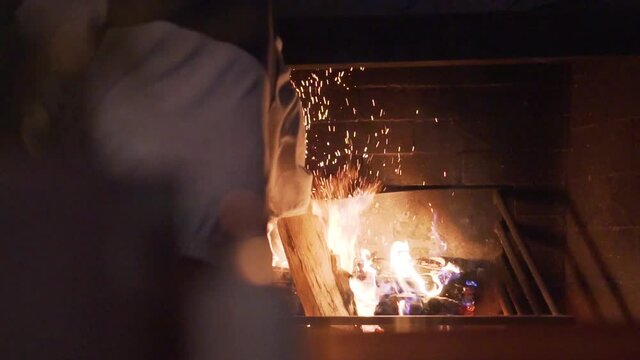 man putting wood log on large open fire at night - slow motion close up