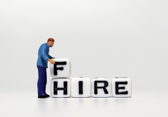 A miniature man who is changing the word HIRE to the word FIRE. The concept of fire and hire. 
