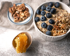 Healthy breakfast bowl: oatmeal with blueberries, nuts and honeycomb piece. Oat flakes with berries and walnuts.