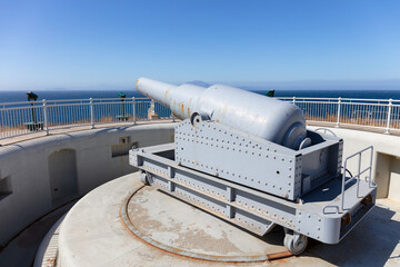 A rotatable gray painted cannon on the southern tip of Gibraltar in summer in sunshine. The gun is aimed at the sea. The African coast can be seen in the background.