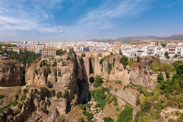 Fototapeta na wymiar Impressive panoramic view from the air of the Andalusian city of Ronda with sunshine and blue skies in summer. In the middle the famous bridge with a waterfall.