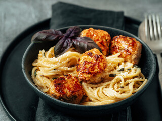 Zucchini Parmesan Meatballs with Pasta Carbonara in black craft plate over gray background. Close up view of creamy carbonara with copy space left