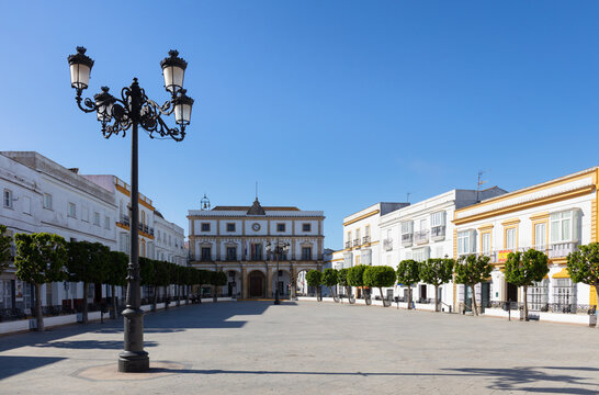 The town hall at the end of the historic market square in the historic mountain village of Medina-Sidonia in Andalusia in southern Spain with green trees. The houses are all painted white.
