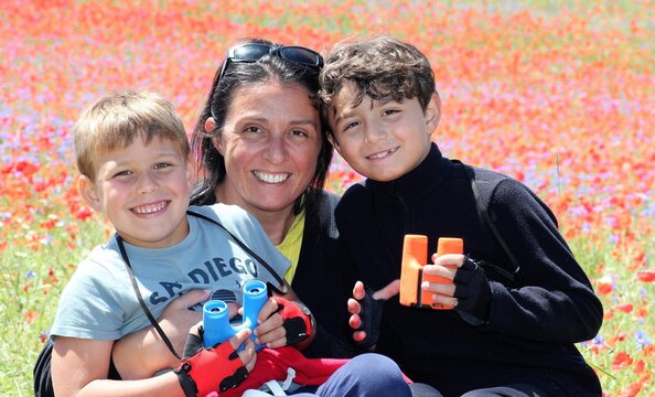 Retrato al natural de familia, madre y dos ni&ntilde;os con prism&aacute;ticos y un mar de flores al fondo