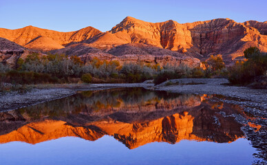 Ridges of the Charyn canyon are reflected in the calm water of the riverside backwaters at sunset; Charyn river in autumn season