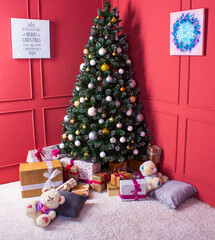 Christmas tall decorated tree against the background of red walls of the room and gift boxes nearby