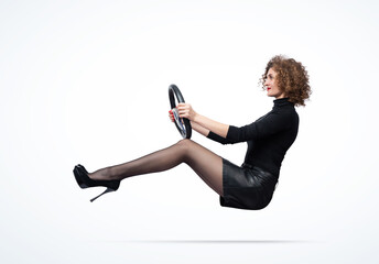 Young happy pretty girl in a black turtleneck, leather skirt with high heels, rides a car holding...