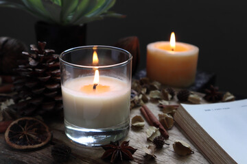 aromatic scented candle glass is lighting on the wooden holder on black wooden table with dried flowers , herbs and spices pinecone in the living room during Christmas party
