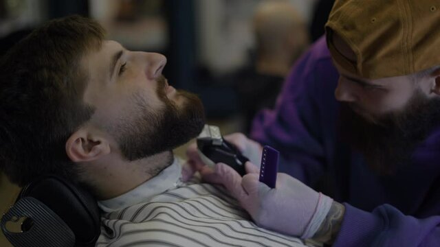Bearded male client in a barber shop. Barber cuts it neatly