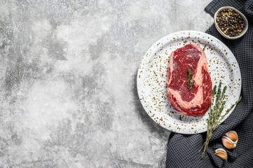 Obraz na płótnie Canvas Raw fresh meat Ribeye Steak with seasoning on cutting board. Rib eye beef steak. gray background. top view. Copy space