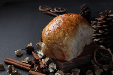 homemade whole grains wheat bread is on the wooden table with cinnamon stick, anise star, potpourri, dried slice lemon, and pinecone in the dark kitchen of the cottage
