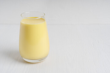 Ayurvedic Indian golden turmeric milk or haldi doodh which is source of antioxidants and anti-inflammatory compounds served in drinking glass on white wooden background. Image with copy space