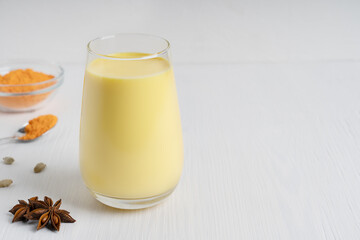 Ayurvedic Indian golden turmeric milk or haldi doodh which is source of antioxidants and anti-inflammatory compounds in drinking glass with anise and curcuma on wooden table. Image with copy space