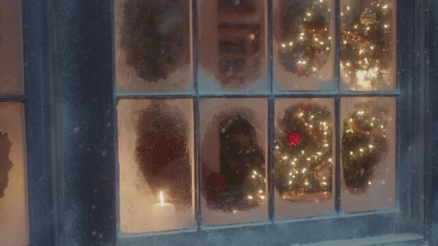 A lit christmas tree is visible through the snow frosted window panes