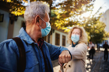 Senior friends with protective masks on standing outdoors and greet with their elbows. Although it's corona outbreak, we have friends.