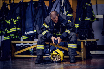Young attractive fireman in protective uniform sitting in fire station and waiting for other...