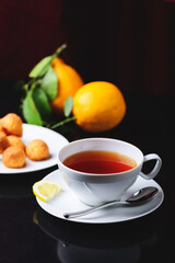 White glass cup with black, red tea with lemon on a dark glass table.