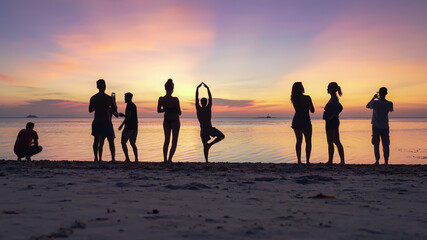 Silhouettes of people on the sandy beach enjoying the sunset and taking pictures on smartphones against the background of the sea