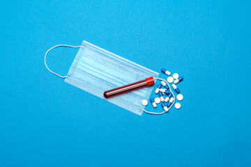 Protective medical face masks, test tube with blood sample and pills on a blue background - Top view with copy space