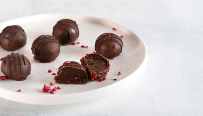 Homemade chocolate sweets with sublimated raspberries on white plate. One candy cut in half. Side view.