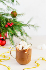 Hot chocolate with coconut milk and carob in a glass mug on the background of a Christmas tree.