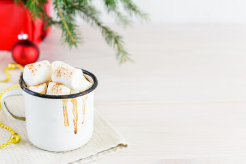 Hot chocolate on coconut milk with marshmallows and cinnamon in a white mug on the background of a Christmas tree. Horizontal orientation, copy space.