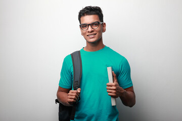 Happy young student of Indian origin carrying shoulder bag and a book