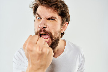 Emotional bearded man in a white t-shirt gestures with his hands light background