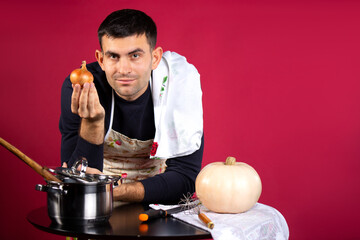 A man prepares food at home in the kitchen and poses with an onion. Photo on a pink background with...