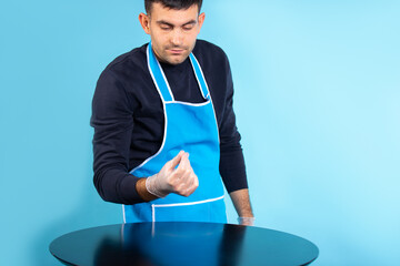A disgruntled man in rubber gloves checks the amount of dust on the table. Gender stereotype. Photo...