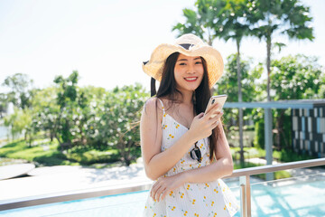 Beautiful traveler woman wear hat using smartphone at hotel balcony